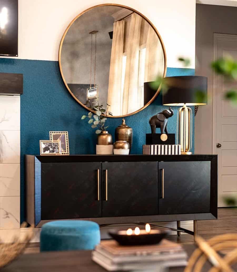 Modern decor with teal accent wall, black sideboard, gold-framed mirror, and elegant gold accents.