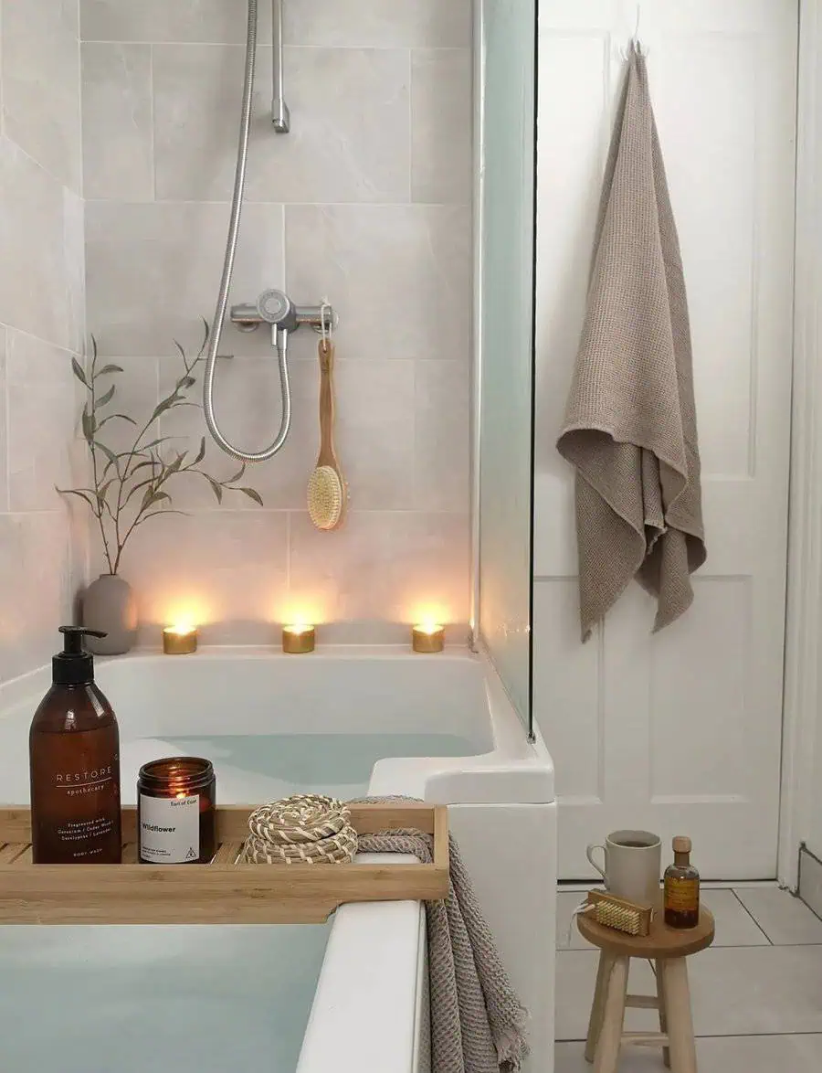 Small luxury bathroom with bathtub, bamboo tray, candles, and cozy spa-like decor.