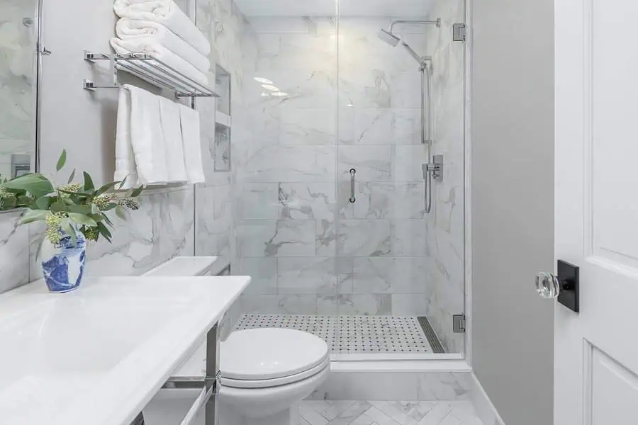 Small luxury bathroom with marble tiles, glass shower, chrome fixtures, and elegant vase decor.