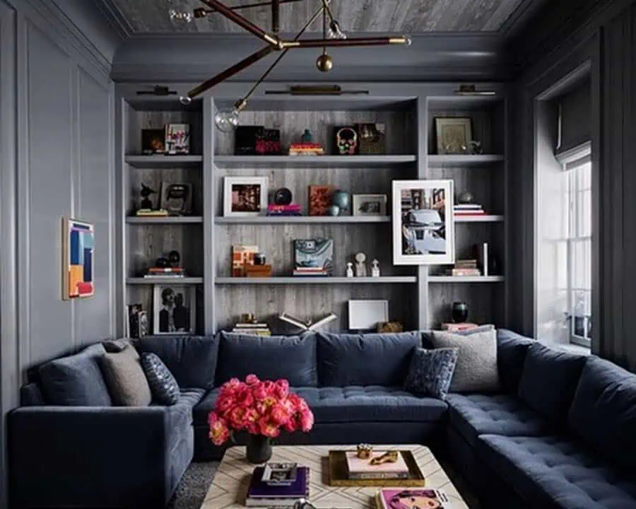 Space-saving den with built-in shelves, navy sectional sofa, modern chandelier, and compact decor.