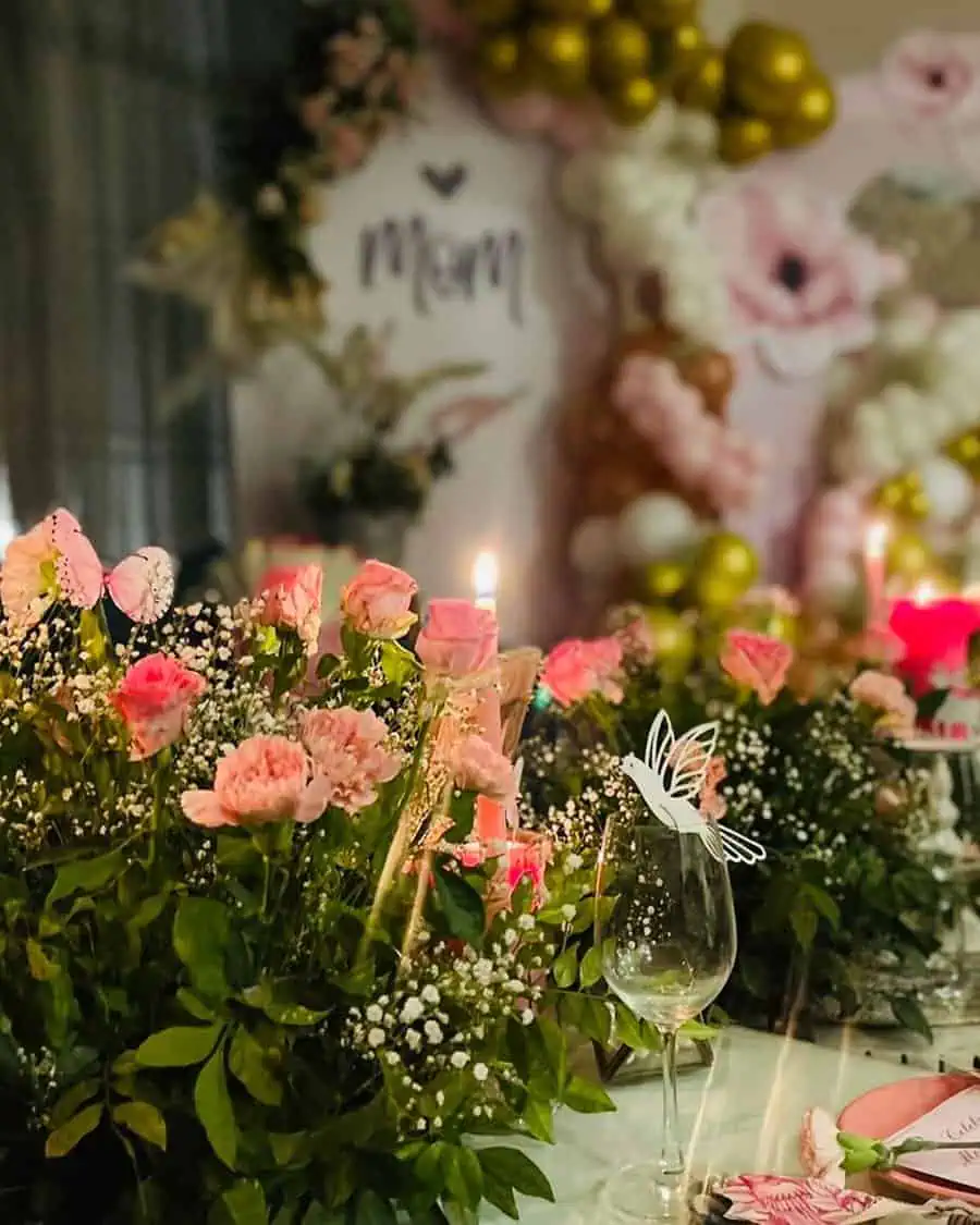 Elegant birthday setup for mom with pink flowers, greenery, candles, and decorative table settings.