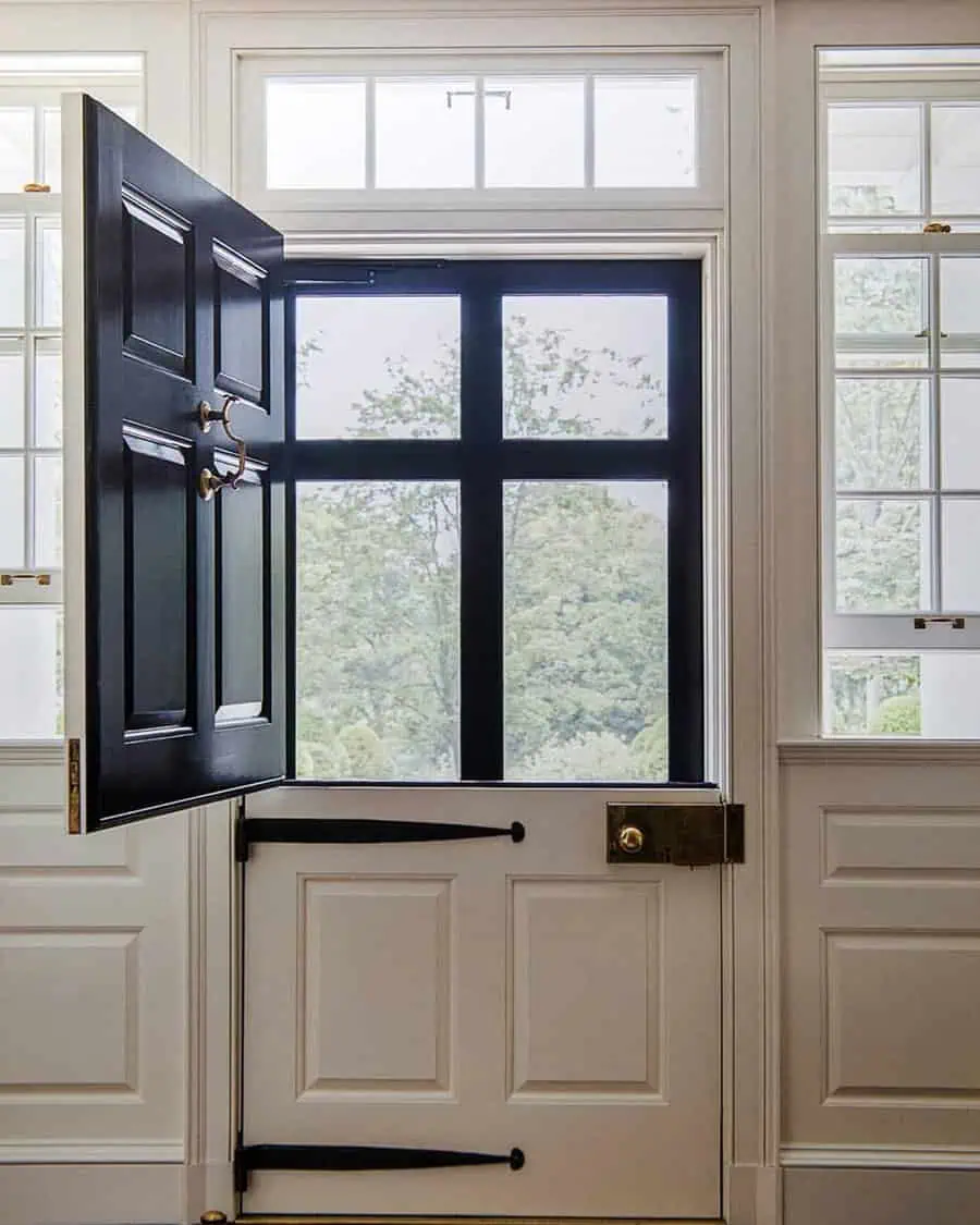 Black and white Dutch door with brass hardware, transom windows, and a scenic outdoor view.