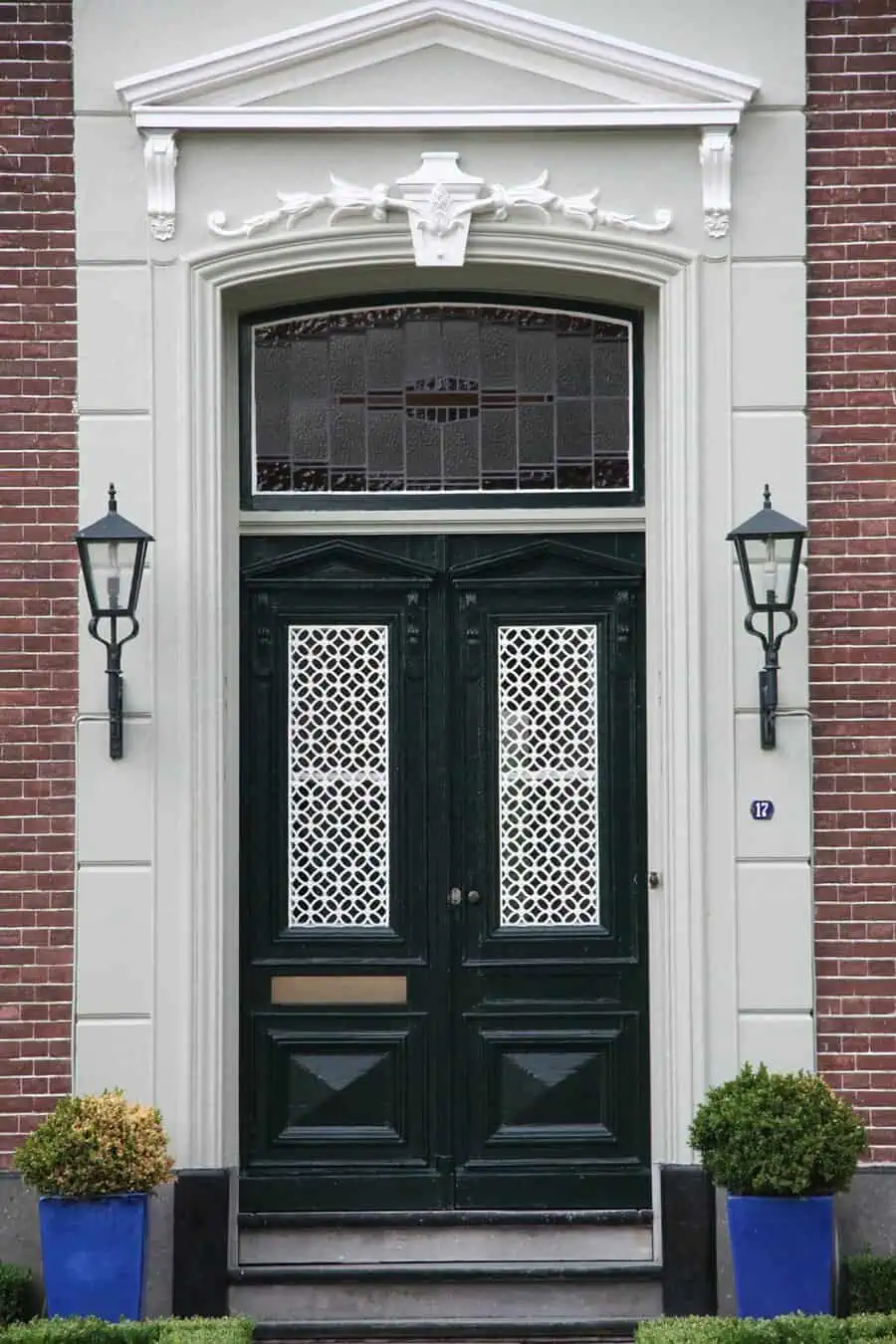 Elegant dark green double doors with intricate white lattice panels and decorative transom.