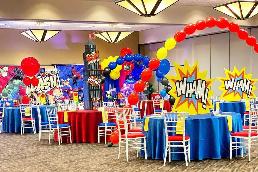 Superhero birthday party with comic-style decorations, balloon arches, and themed table settings.