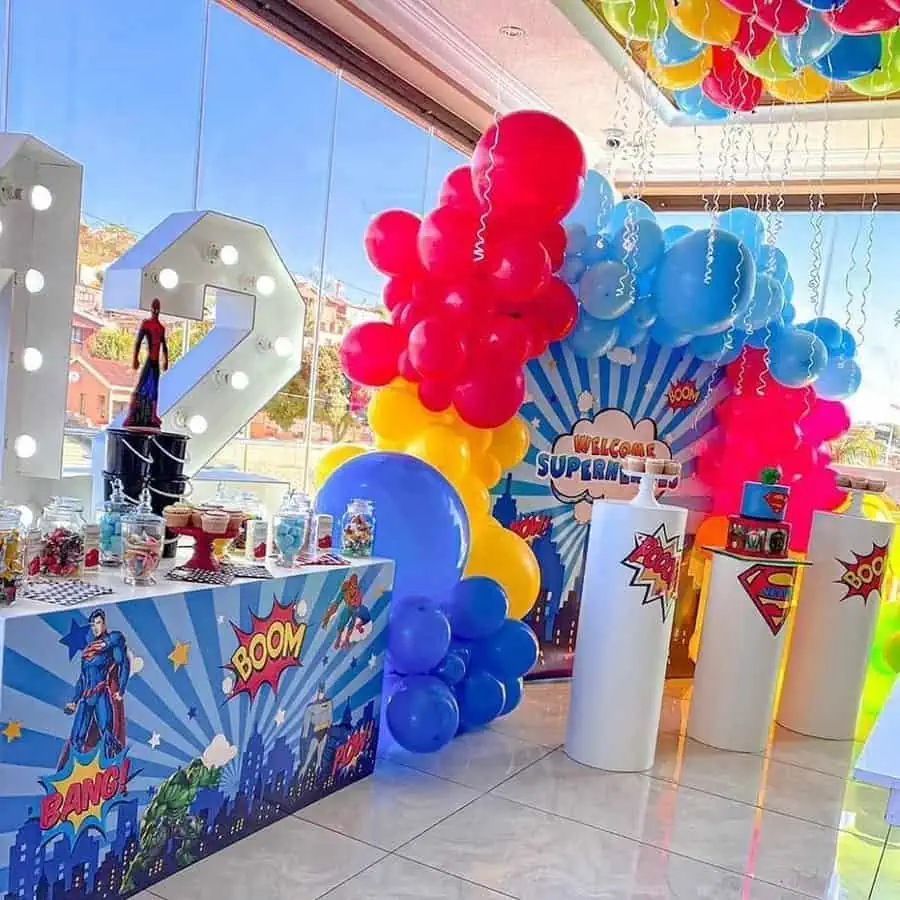 Superhero-themed birthday setup with comic-style decor, colorful balloons, and candy table