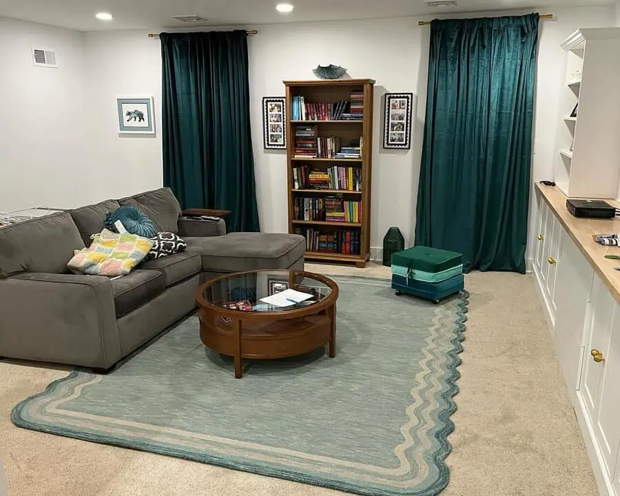 Cozy living room with teal floor-length curtains, a gray sectional sofa, and a classic wooden coffee table.