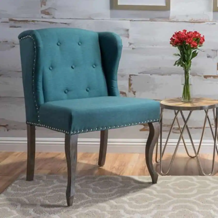 Teal wingback chair with studded accents and elegant legs.