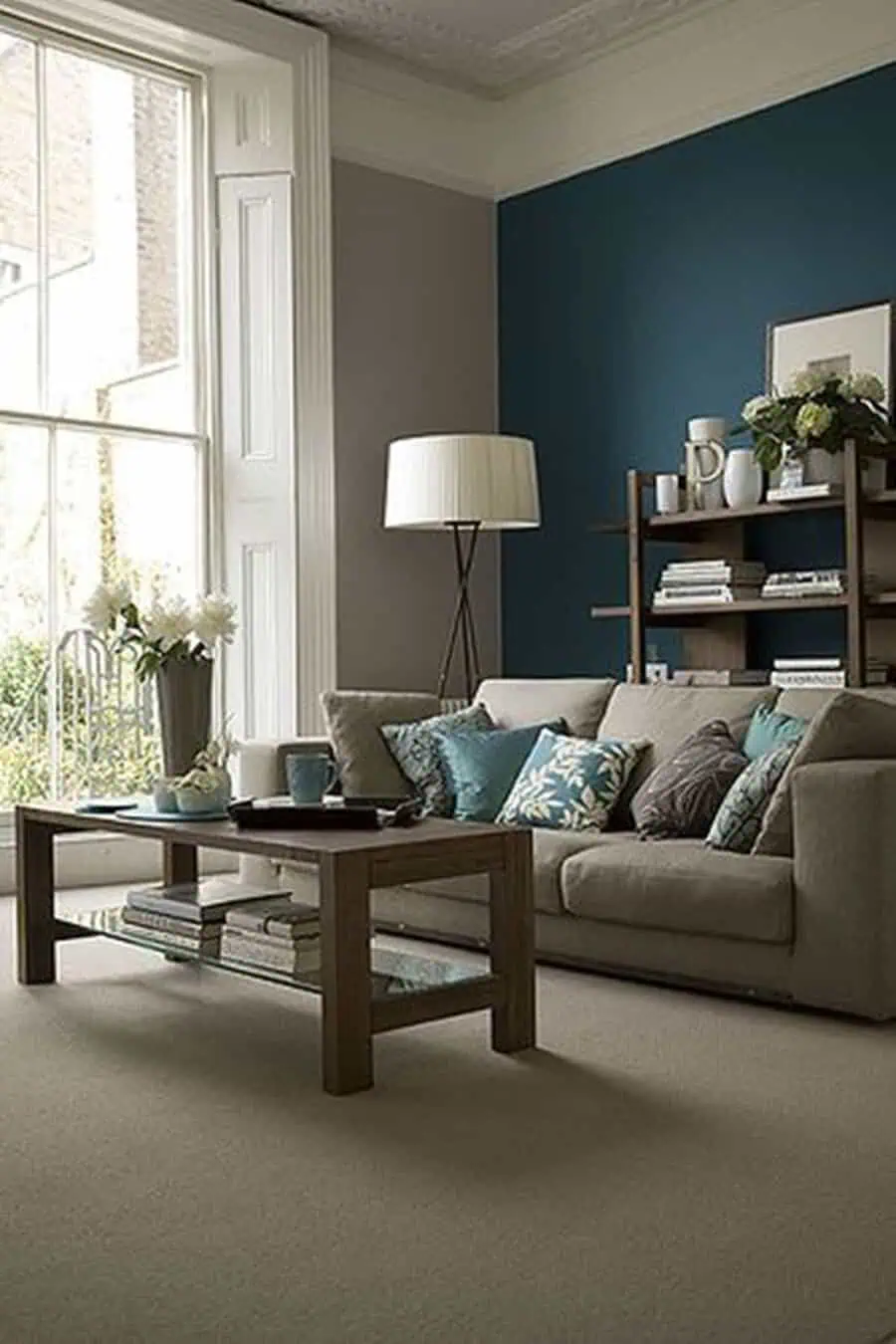 Teal living room with beige sofa, floral accent pillows, wooden coffee table, and floor lamp.