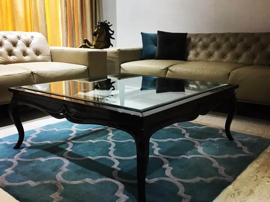 Elegant living room featuring a teal Moroccan-style rug, a sleek glass-top coffee table, and tufted beige sofas for a luxurious ambiance.