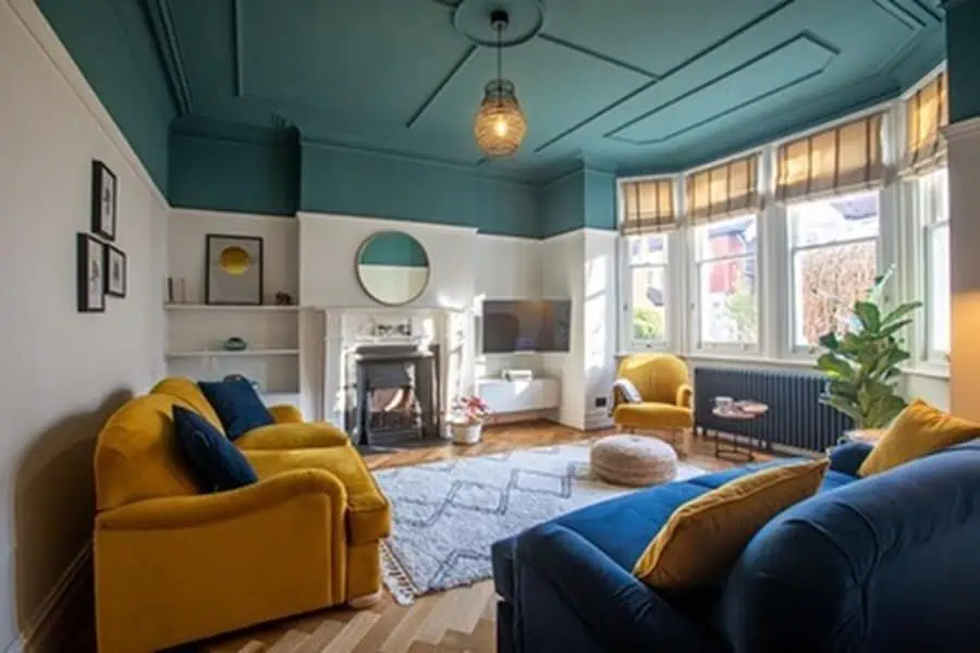 Teal-painted ceiling paired with bold yellow and navy furniture in a stylish living room.