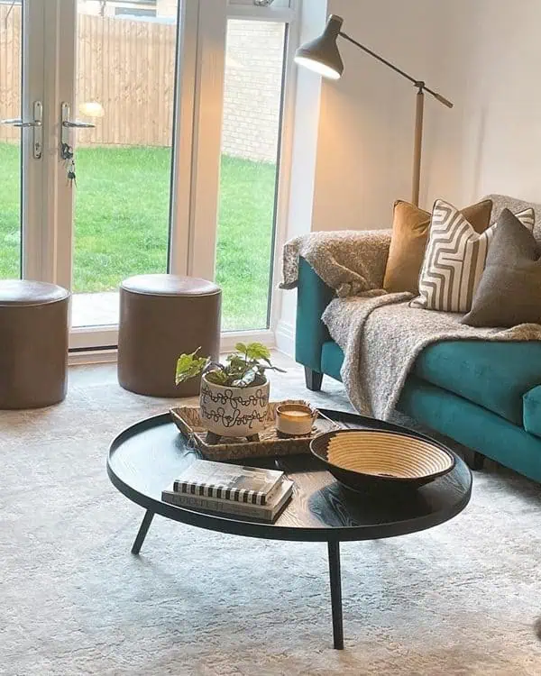 Cozy living room with teal sofas, a light area rug, a black round coffee table, and large patio doors letting in natural light. 