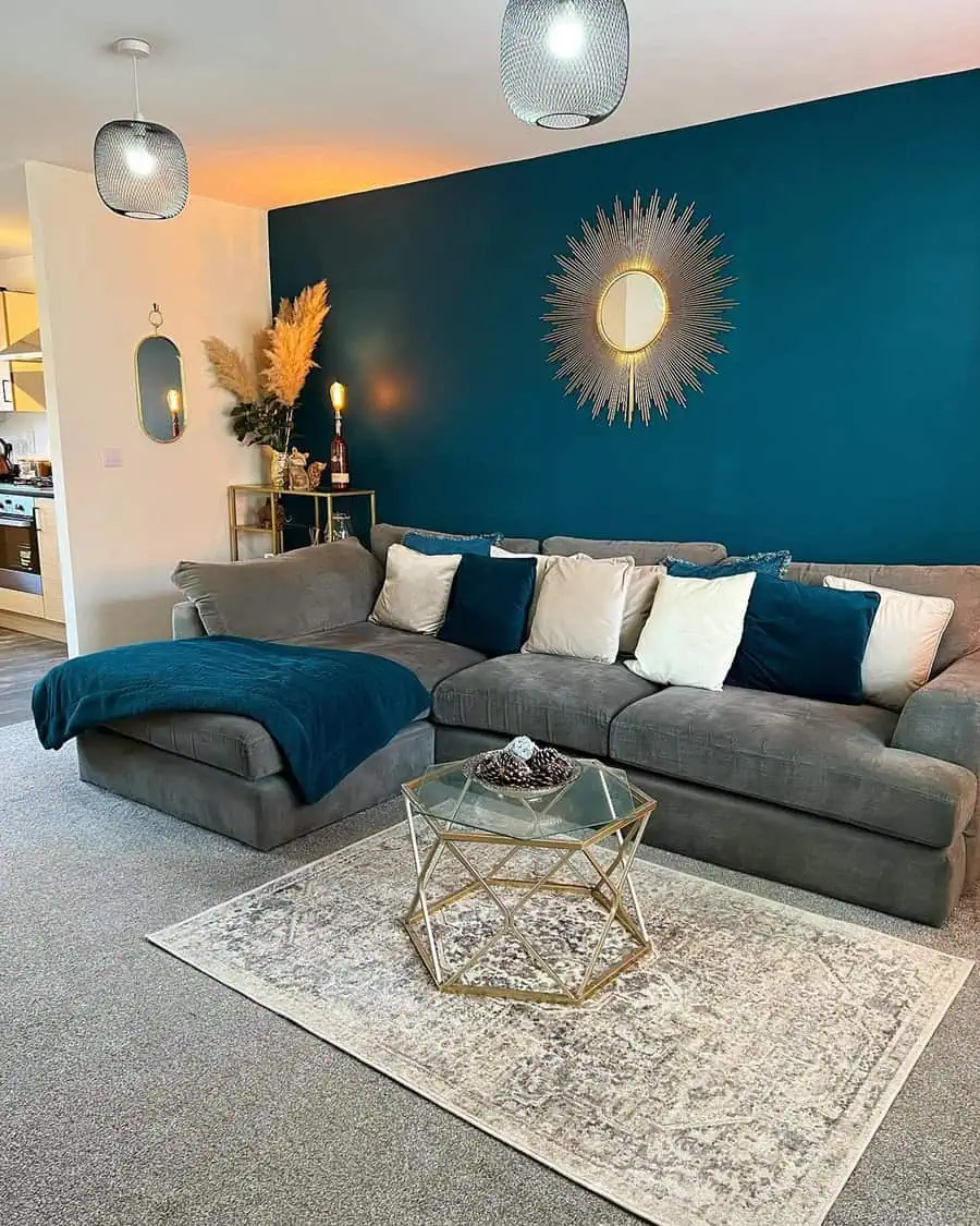 Sophisticated living room featuring a bold teal accent wall, gold sunburst mirror, and cozy throw pillows.