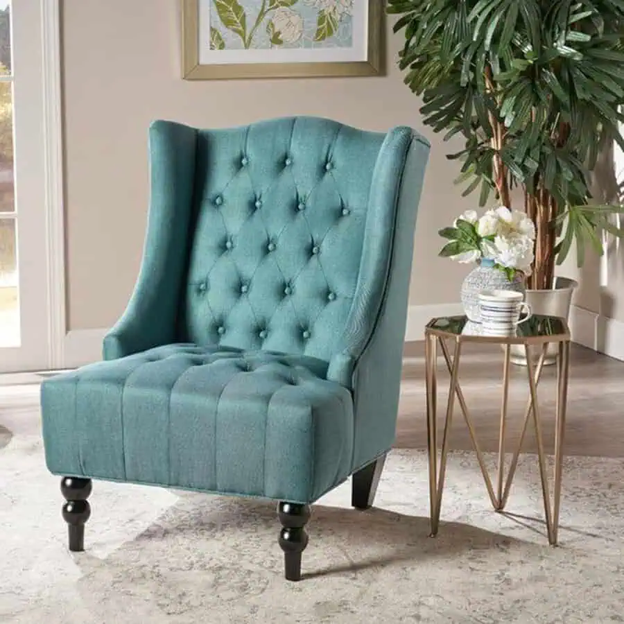 Teal wingback chair with tufted design and a sleek side table.