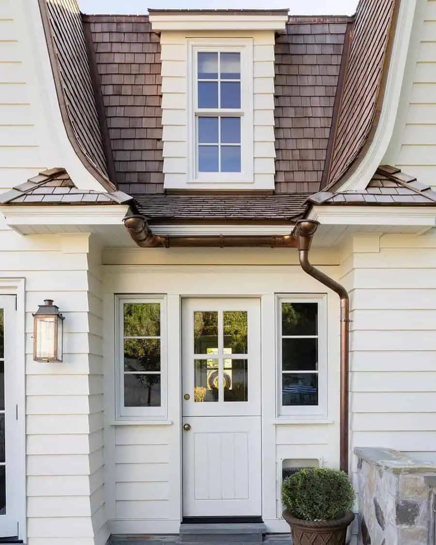 Charming white Dutch door with glass panes, surrounded by windows and a stone-accented entryway.