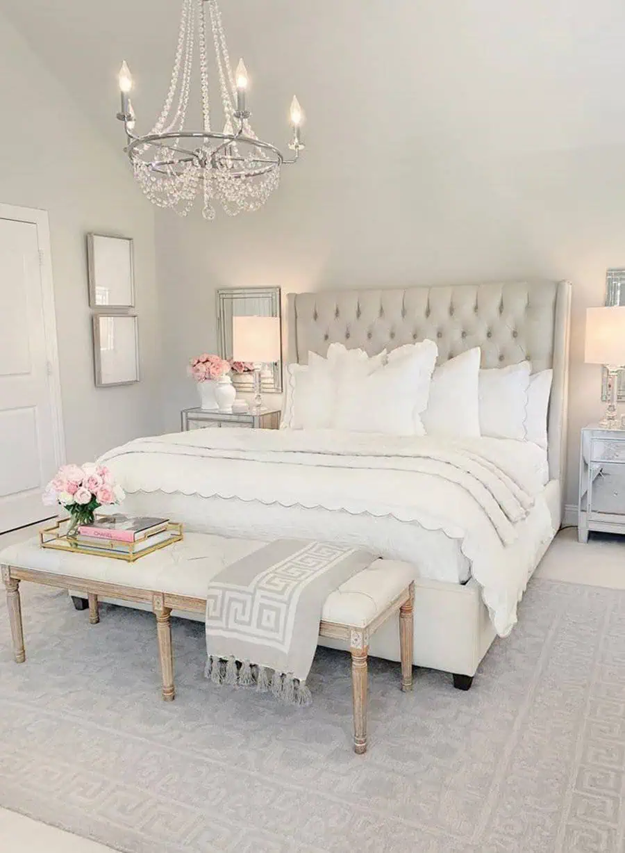 Elegant bedroom with tufted headboard, crystal chandelier, and soft white bedding decor.