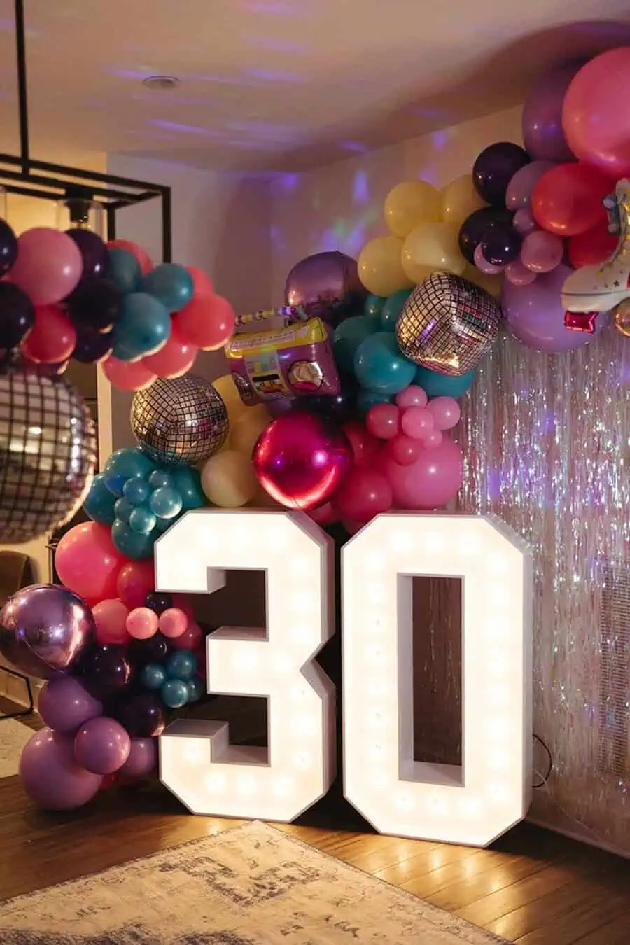 Colorful balloon decor with disco balls and illuminated "30" for a vibrant 30th birthday.