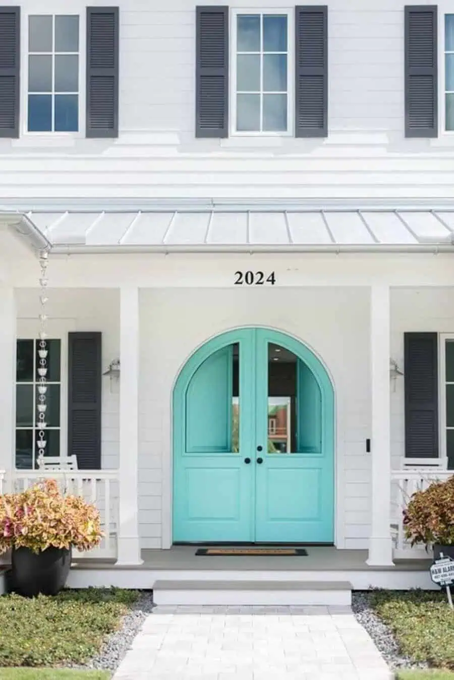 Turquoise arched Dutch doors on a white facade with black shutters and potted plants.