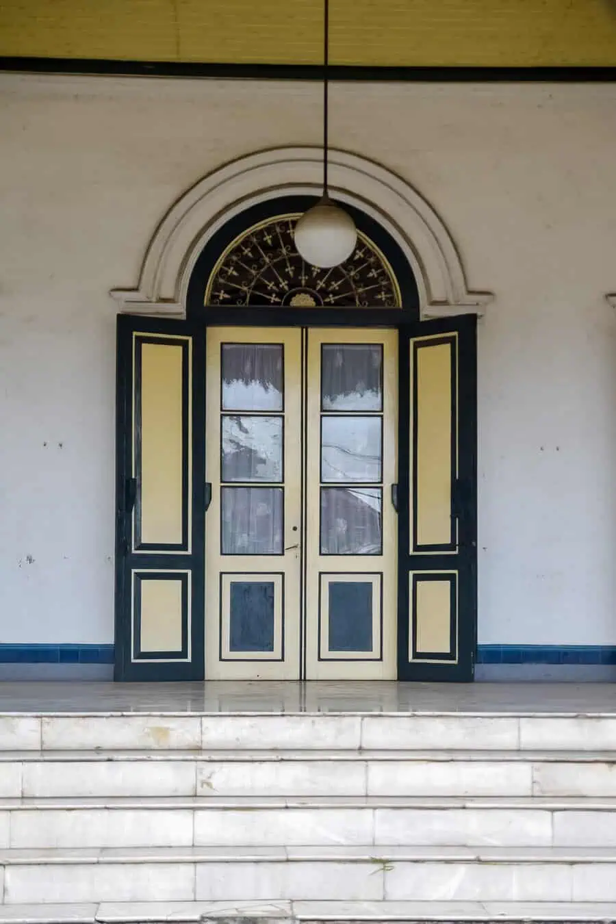 Vintage Dutch door with arched transom and yellow-black detailing on marble steps.