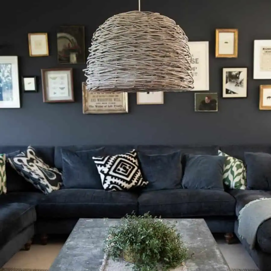 Eclectic living room with wicker pendant light, dark sectional sofa, and gallery wall decor.