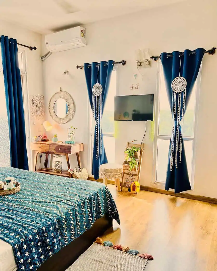 Eclectic bedroom with blue curtains, patterned bedding, vintage mirror, and wooden furniture.