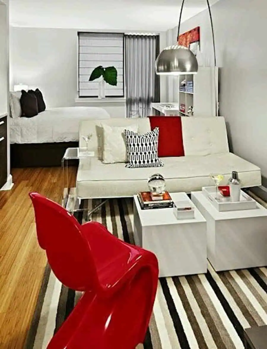 Studio apartment with bold red accents, striped vintage rug, and modern minimalist furniture.