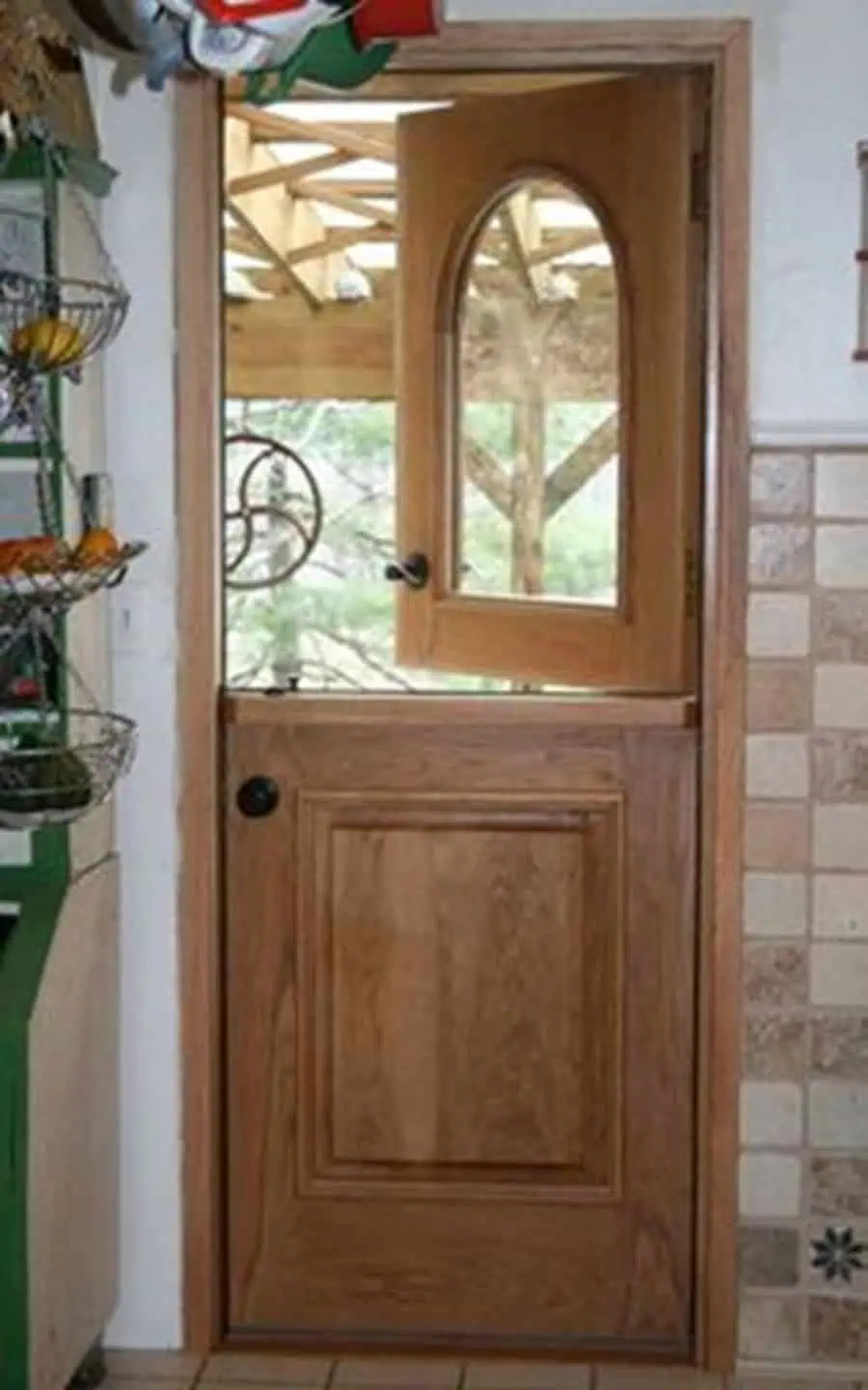 Wooden Dutch door with arched glass panel, tiled wall, and rustic kitchen decor.