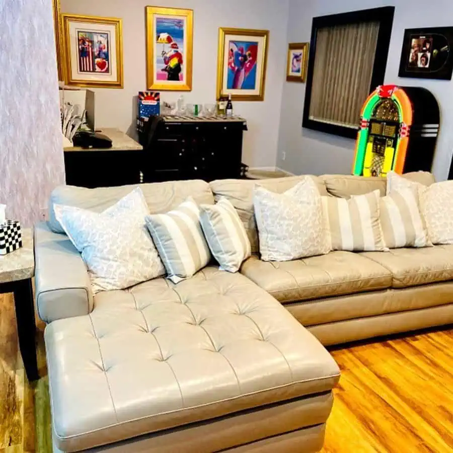 Retro-style den with beige sectional sofa, vibrant wall art, jukebox, and wood flooring.