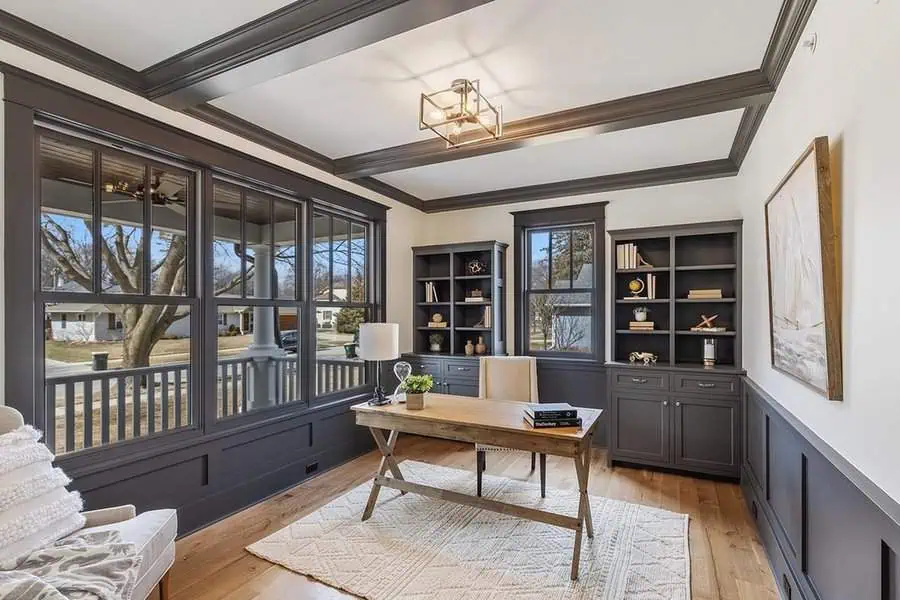 Bright den with large windows, built-in dark shelves, wooden desk, and elegant ceiling design.