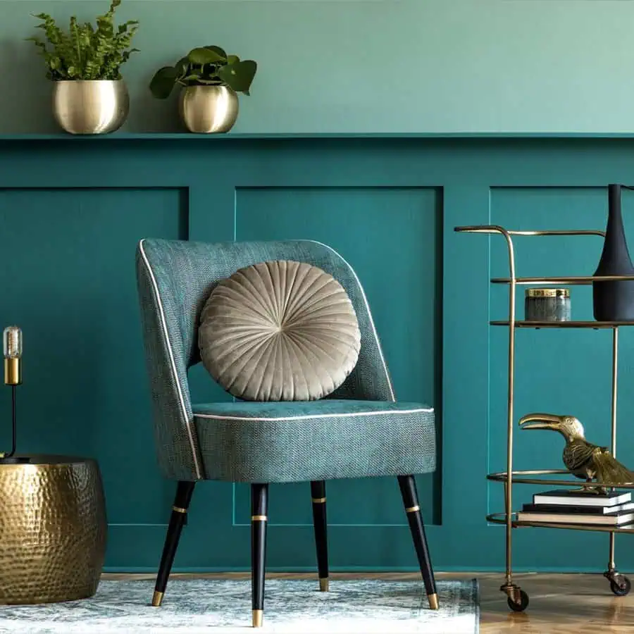 Teal accent wall with a textured chair, warm brown decor, gold accents, and indoor plants.