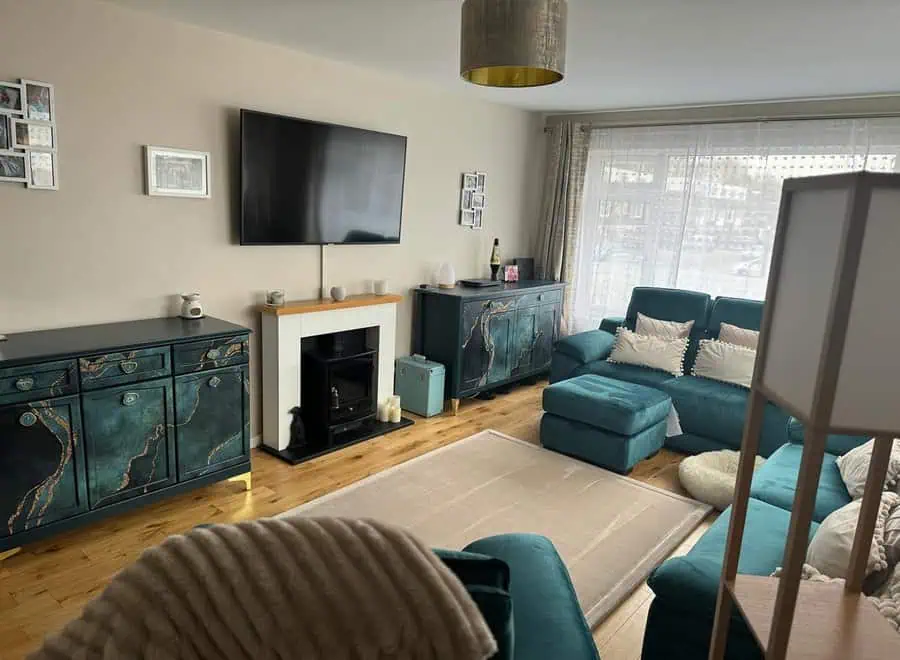 Living room with teal furniture, warm brown wood floors, neutral walls, and decorative teal cabinets.