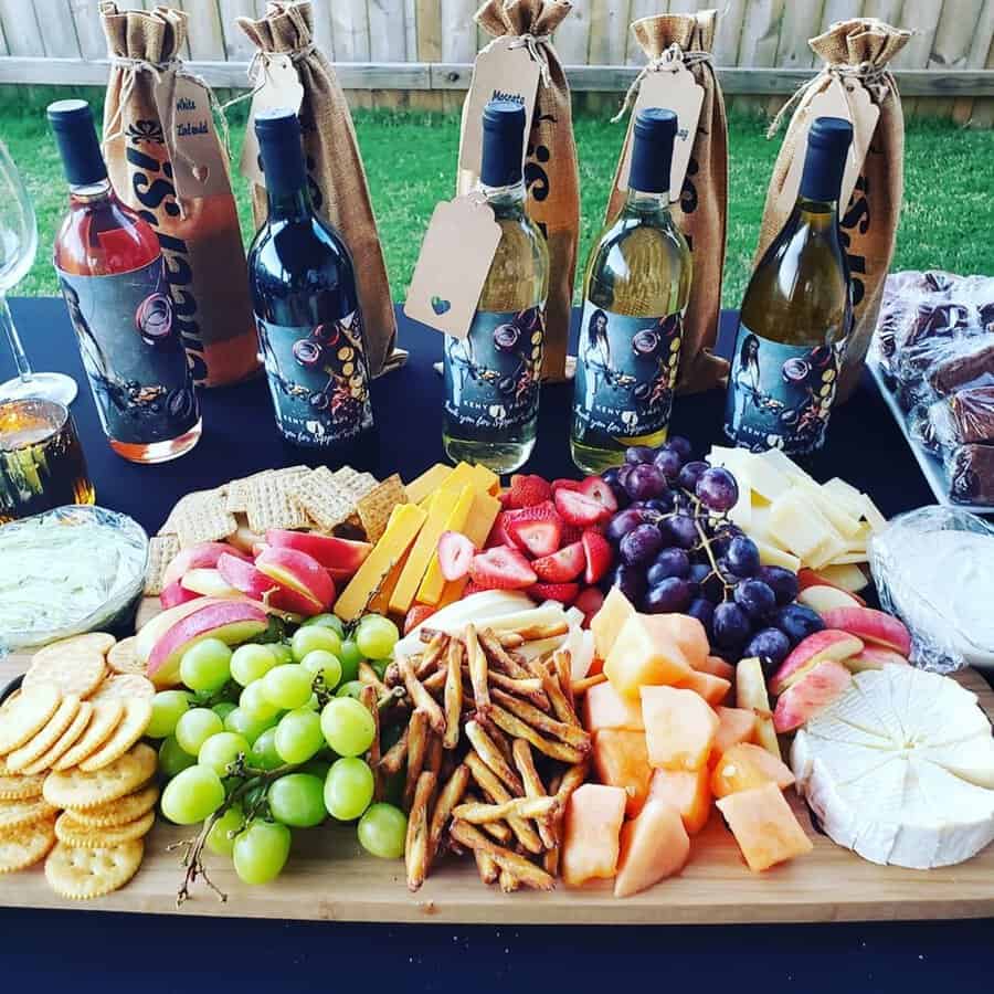 Outdoor wine and cheese birthday party with fruit, crackers, and bottles of wine.