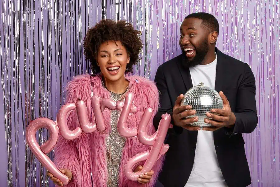 Two friends celebrating a 20th birthday with party balloons and a disco ball backdrop.