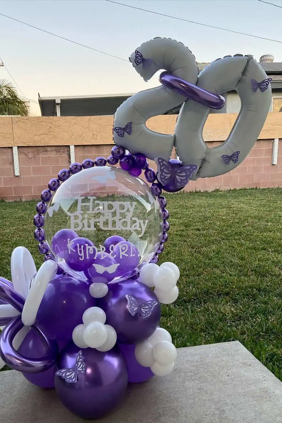 Purple and silver "20" balloon display with butterflies and personalized birthday message.