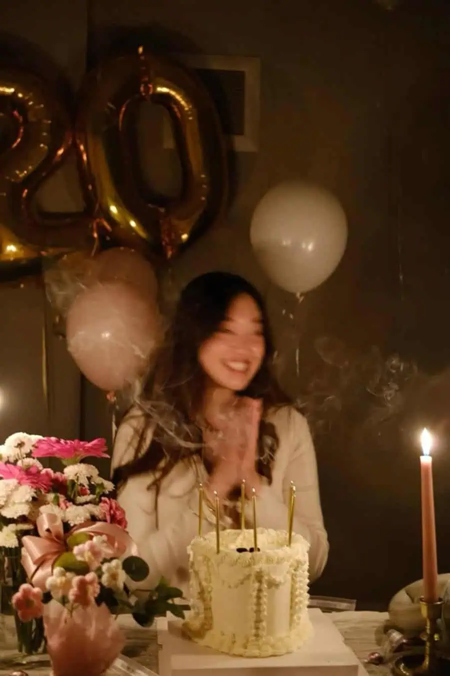 Intimate 20th birthday celebration with a floral cake, gold candles, and "20" balloons.