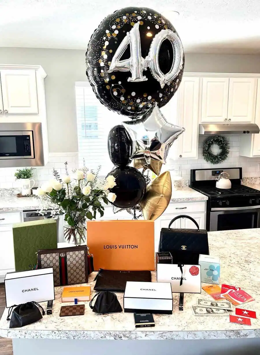 Luxury 40th birthday gifts display with designer items, balloons, and fresh white roses.