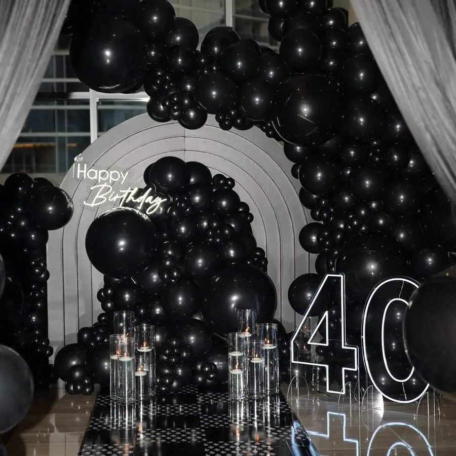 Sophisticated 40th birthday setup with black balloons, neon "Happy Birthday" sign, and candles.