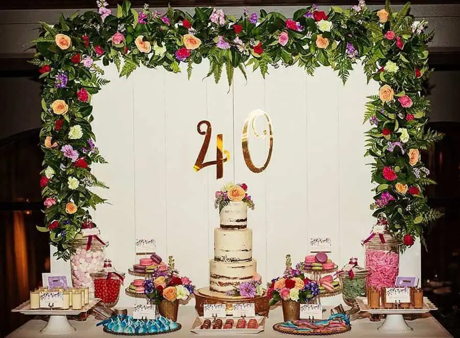 Elegant dessert table with floral arch, naked cake, and gold "40" sign for a 40th birthday.