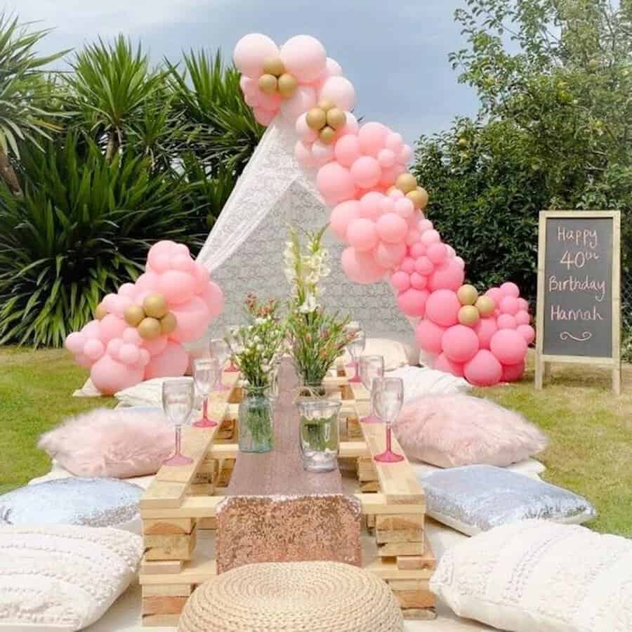 Chic outdoor picnic setup with pink and gold balloons, teepee, and personalized chalkboard for 40th birthday.