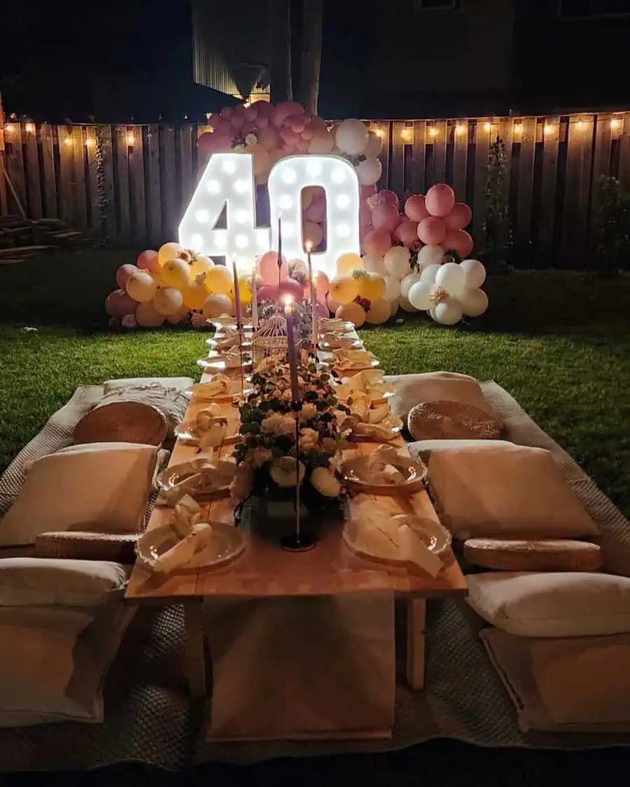 Outdoor 40th birthday dinner setup with illuminated "40" sign, pastel balloons, and elegant table decor.