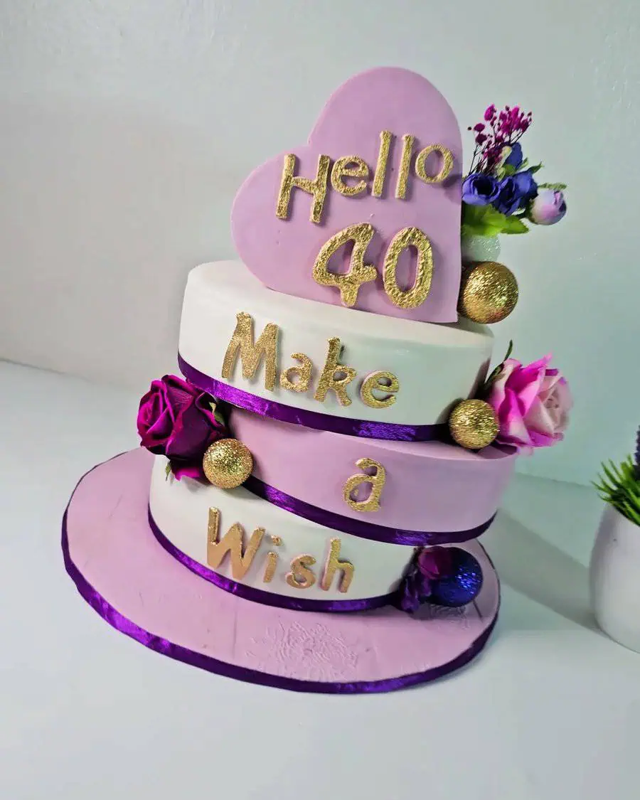 Whimsical 40th birthday cake with heart topper, gold accents, and floral decorations.