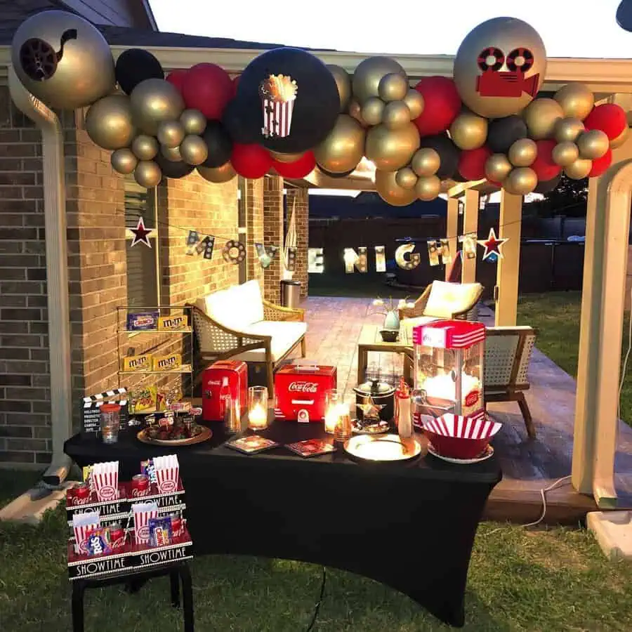 Movie night-themed 40th birthday setup with popcorn, candy, and gold and red balloon garland.