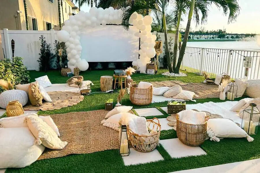 Boho-inspired outdoor movie setup with cozy seating, white balloon arch, and lake view for 40th birthday.