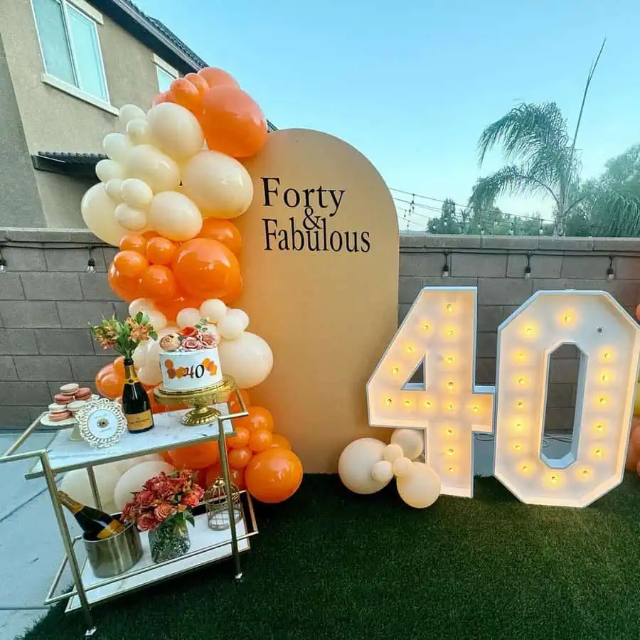 "Forty and Fabulous" outdoor 40th birthday setup with orange balloons and illuminated "40" sign.