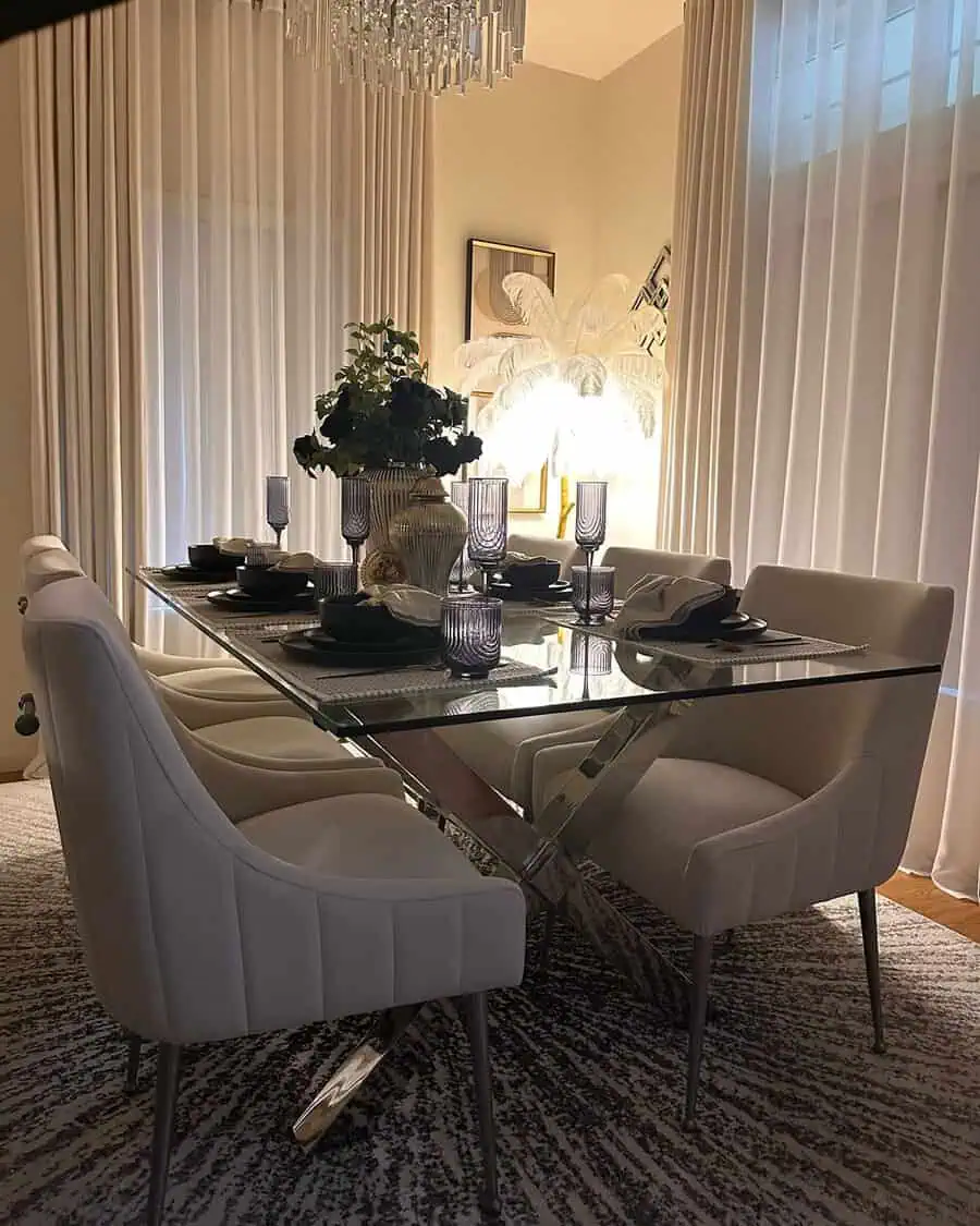 Luxurious dining room with a glass table, white chairs, and crystal chandelier lighting.