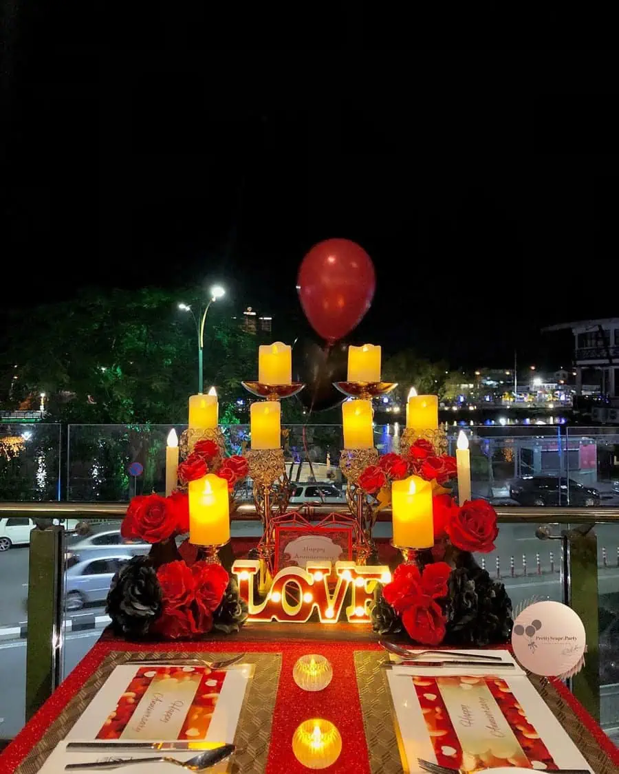 Romantic candlelit anniversary dinner setup with roses and a glowing "LOVE" sign.