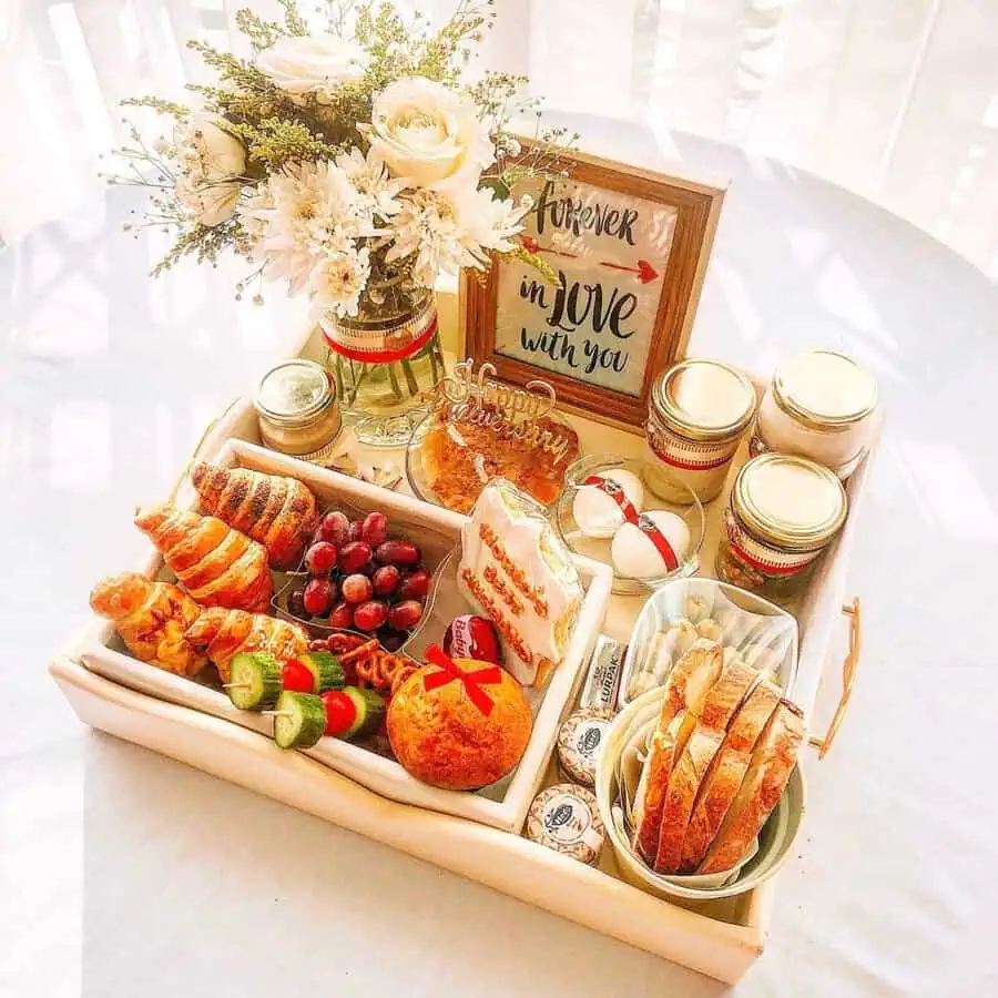 Anniversary breakfast tray with croissants, bread, fruits, flowers, and a "Forever in Love" sign.