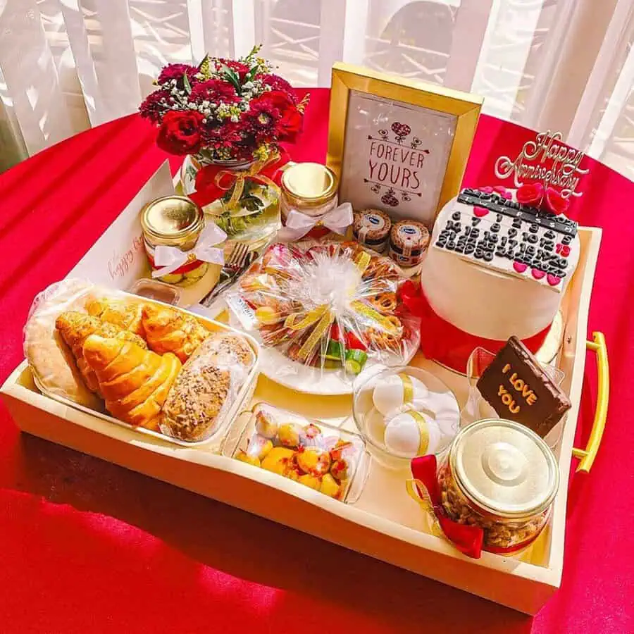 Anniversary breakfast tray with pastries, cake, fruits, flowers, and a "Forever Yours" sign.