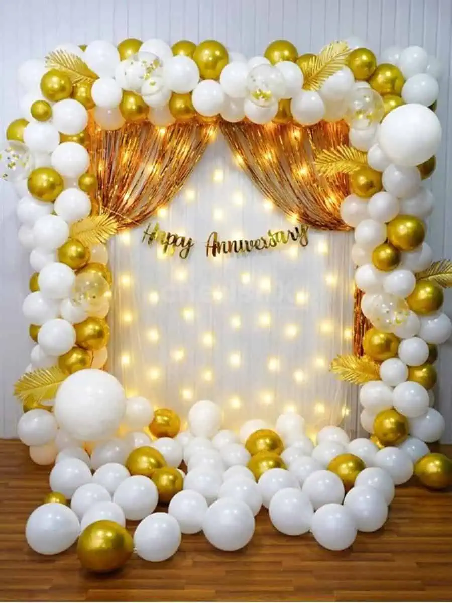 Elegant anniversary backdrop with white and gold balloons, fairy lights, and a "Happy Anniversary" sign.