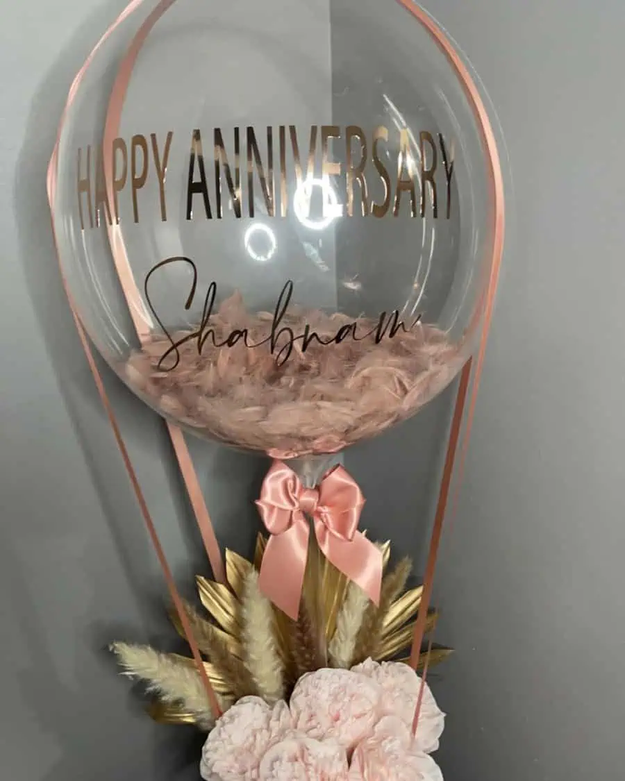 Personalized anniversary balloon with pink feathers, ribbon, and a floral base design.