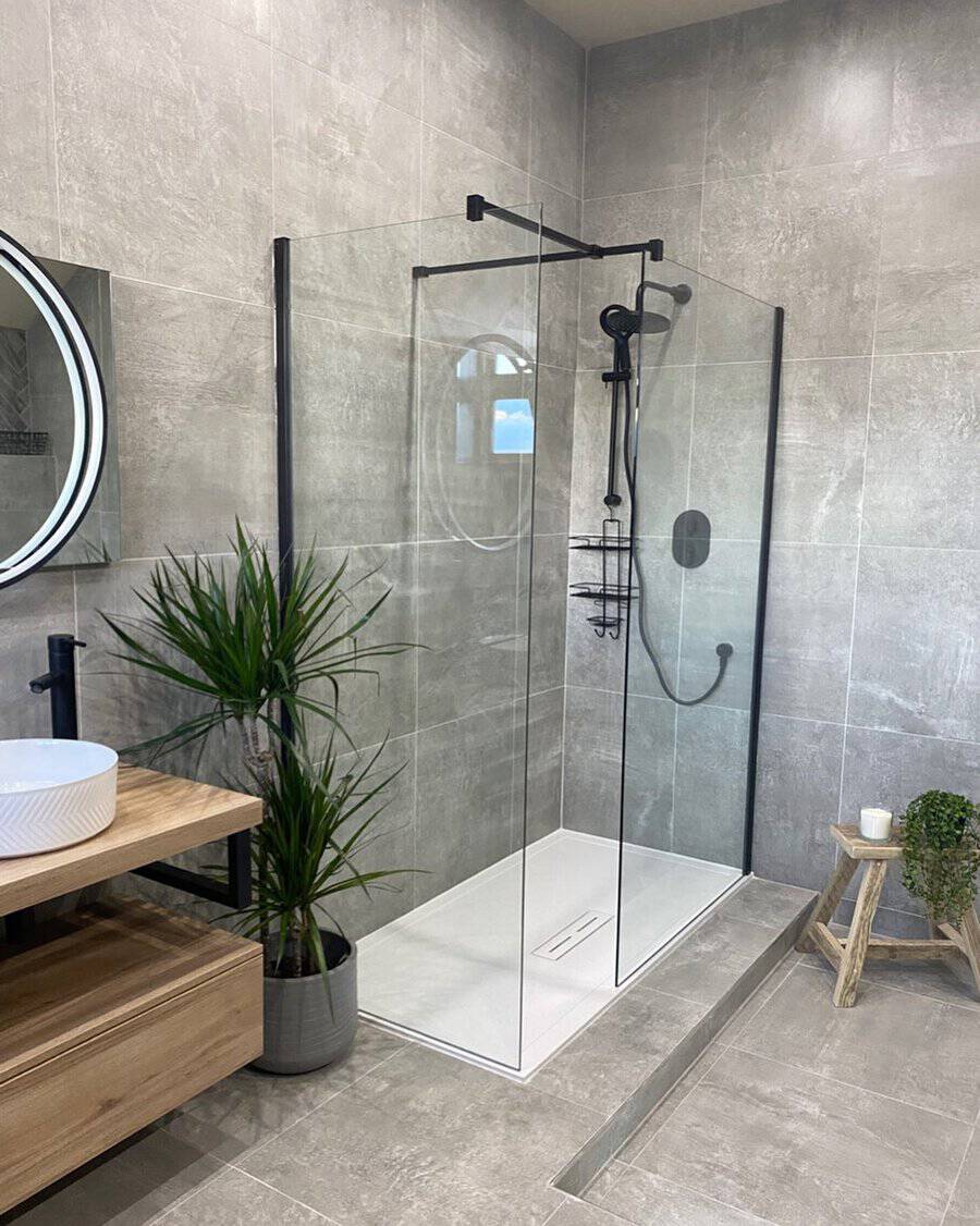 Modern bathroom with light grey tiles, glass walk-in shower, wooden vanity, and potted plant.